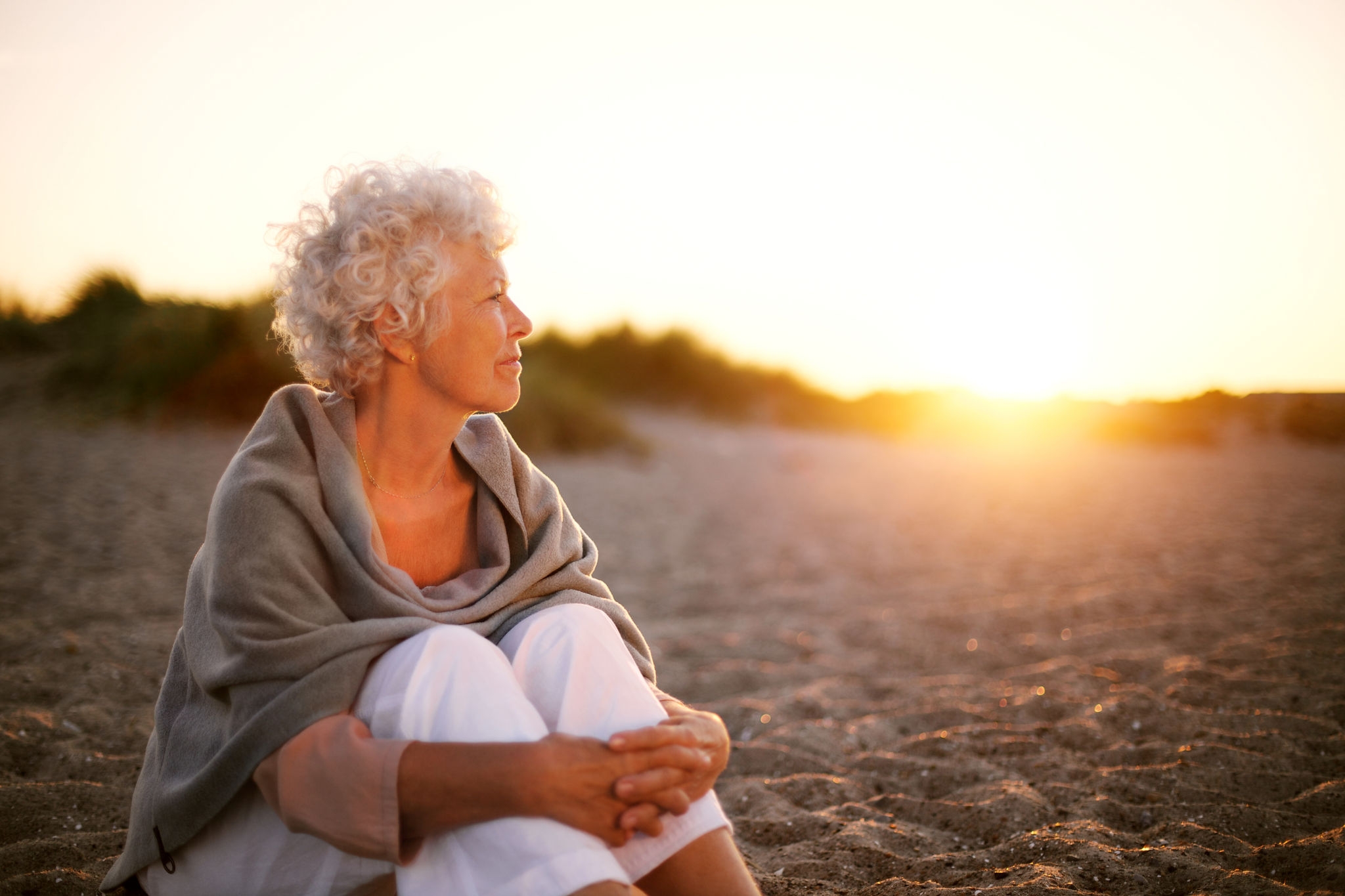 Older woman sitting on beach at sunset