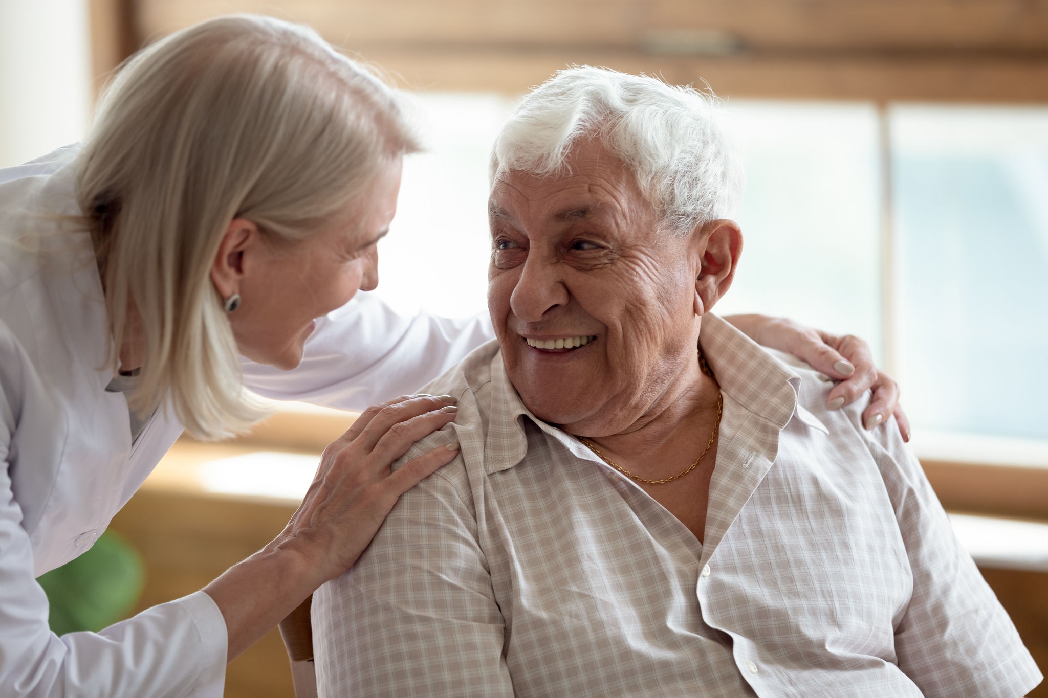 Caring middle-aged female licensed practical nurse in white coat talk to elderly patient 80s man, worker care about old healthcare consumer listens complaints give support, caregiving service concept