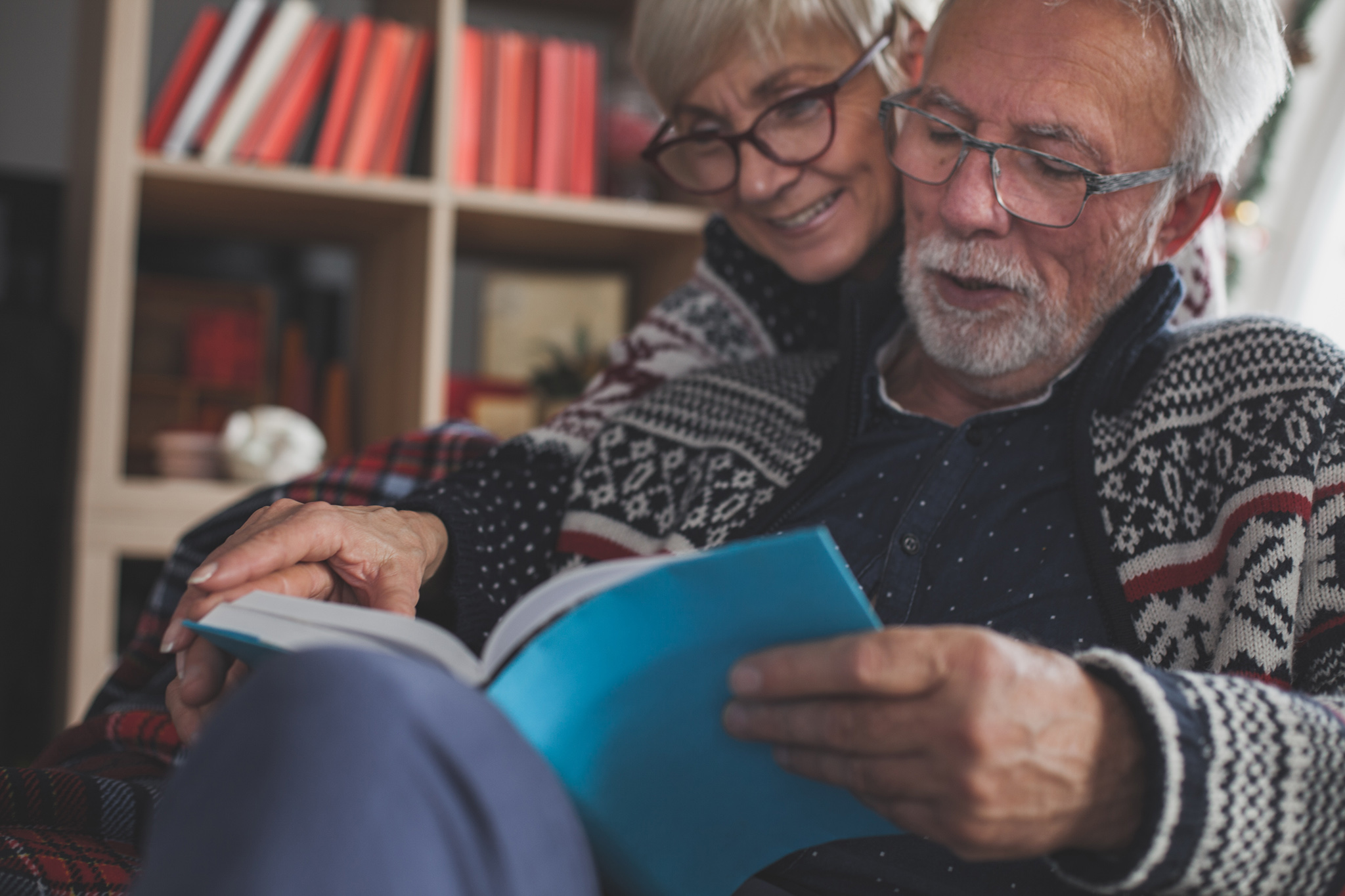 Senior married couple in cozy winters clothes relaxing and enjoying reading a book together.