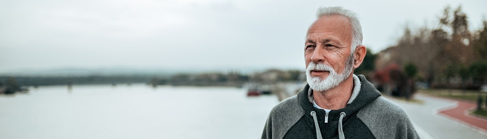 Portrait of a senior sportsman walking near the river in the city.
